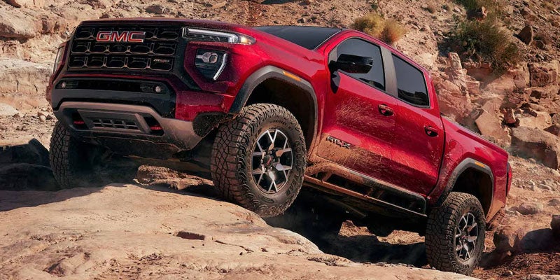 Red 2026 GMC Canyon driving on a rugged off-road trail